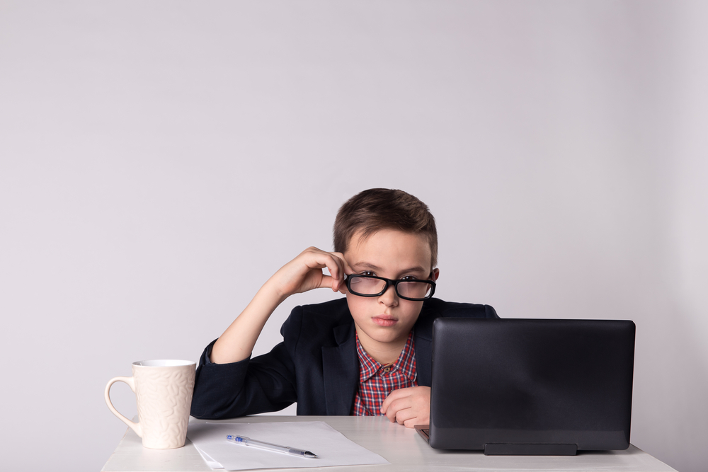 Portrait of young tired business child in suit sitting at the table.