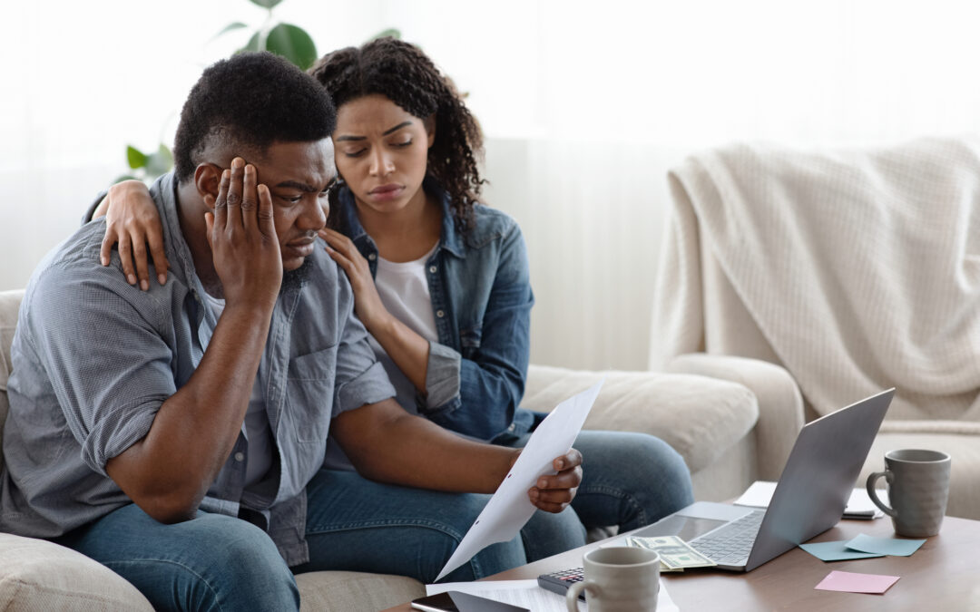 Depressed black couple sitting with paperwork in living room
