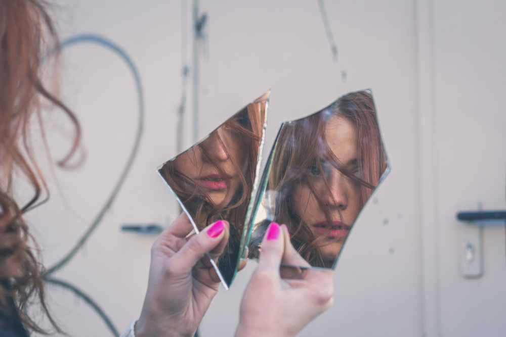 Woman looking at herself in a broken mirror