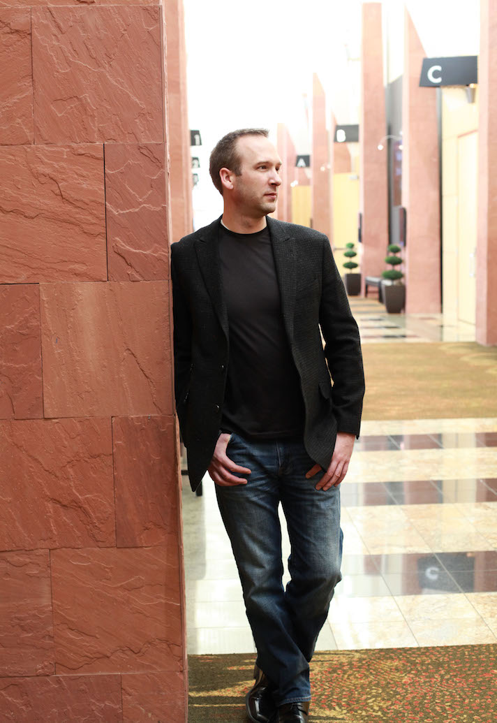 IMG_4950 x1035 Coach Joe Burns in a dark jacket and gray tee smiling at the camera in front of a building